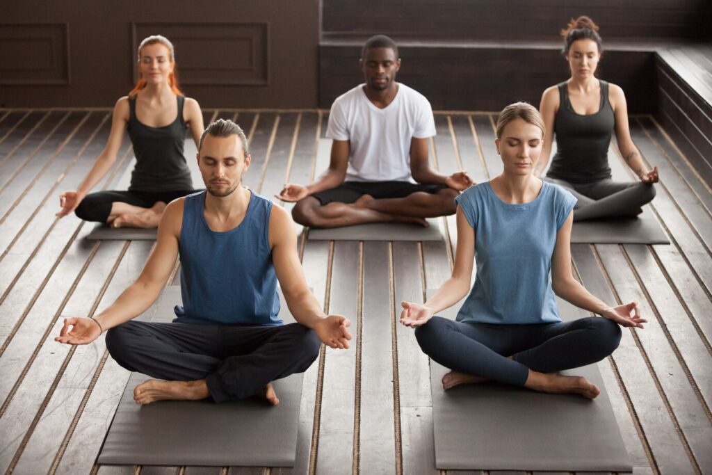 A diverse group of people sitting cross-legged on yoga mats, meditating in a calm and focused manner during a group session.