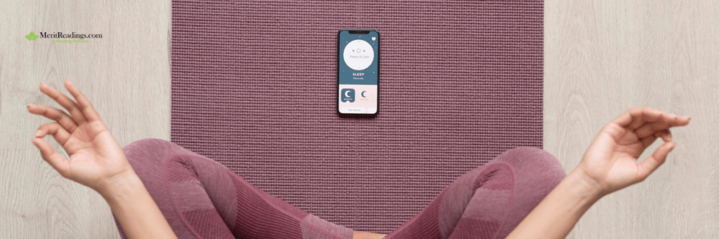 A person sitting cross-legged on a purple yoga mat with hands resting in a meditative mudra. A smartphone displaying a meditation or sleep app is placed on the mat in front of them.