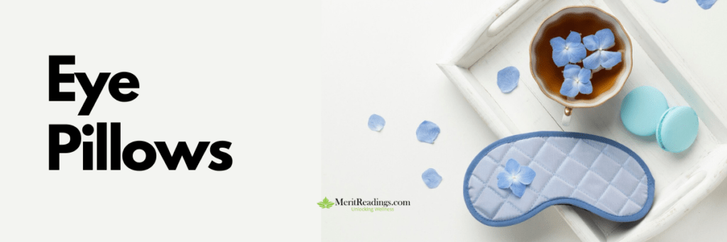 A blue quilted eye pillow with a floral decoration, placed on a white tray alongside a cup of tea garnished with blue flower petals and a macaron. Additional petals are scattered on the surface.