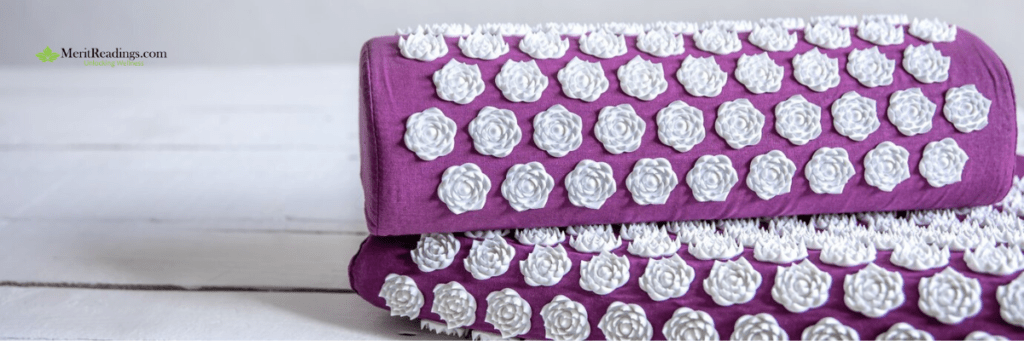 A purple acupressure mat and pillow set with white lotus-shaped spikes, placed on a light wooden surface.

