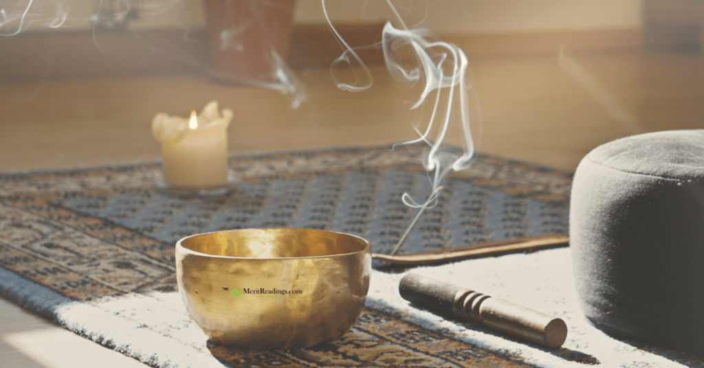 A serene meditation setup featuring a brass singing bowl, a lit candle, incense releasing smoke, and a meditation cushion on a patterned rug.